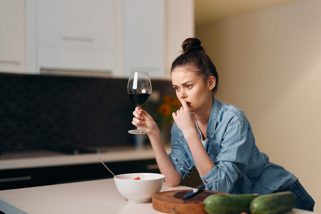 Emotional eating and drinking: Alone at Home: Sad Young Caucasian Woman Holding a Glass of Wine in the Kitchen