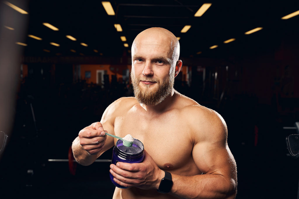 Professional bodybuilder wearing no t-shirt and holding a scoop of protein powder